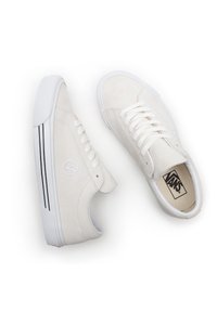 Hvite semskede sneakers med lav profil, med hvite snørebånd, logo-detalj og doble svarte striper på siden. Gummisåle.
