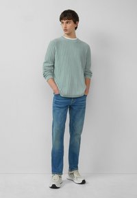 Jasnozielony, żebrowany sweter w połączeniu z niebieskimi dżinsami i jasnymi trampkami. Strój ma luźny krój i casualowy design.