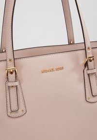Sac fourre-tout en cuir texturé rose poudré avec des sangles à boucle dorée et le logo Michael Kors embossé en or au centre avant.