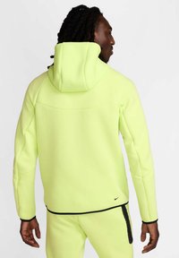 Sudadera de alta visibilidad en color amarillo neón con un ajuste relajado, capucha ajustable y detalles en negro, fabricada con un tejido suave y texturizado.