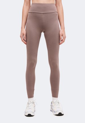 Vue de face d'une personne portant des leggings mauves taille haute, des chaussettes blanches et des baskets blanches sur un fond uni.