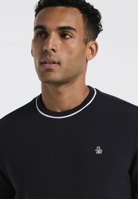 Marineblauwe gebreide trui met een gestructureerde stof, witte accenten op de kraag en een klein pinguïnlogo op de linkerborst.