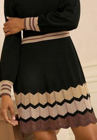 Rochie neagră cu mâneci lungi, prezentând modele în zigzag aurii și maronii la marginea de jos și la manșete, cu accente texturate ribbed.