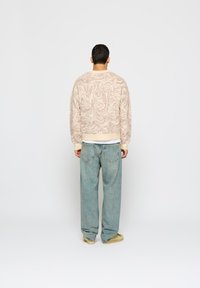 Pulóver v krémovej farbe s mramorovým hnedým vzorom, skombinovaný s voľnými svetlomodrými džínami. Pozor na ribovaný lem a manžety.