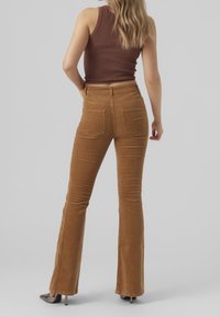 Brown corduroy flared pants with back pockets, high waist, and a soft texture, paired with a fitted brown ribbed tank top.