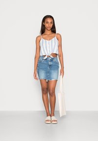 Top cropped azul e branco com riscas, com um laço à frente, combinado com uma saia mini de ganga. A modelo segura uma mala tote bege e usa sandálias claras.
