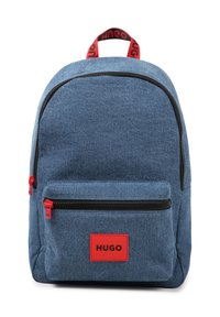 Denim backpack in blue with a front pocket. Features red zippers and an accent strap. Black zipper detailing and a red logo patch.