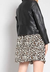 Musta nahkatakki, jossa on istuva malli, yhdistettynä kermaan vivahtavaan leopardi-kuvioituun hameeseen, jossa on röyhelöinen helma ja laskostettu pinta.