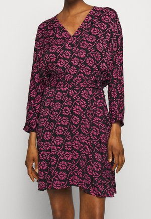 Frau trägt ein schwarzes Kleid mit einem rosafarbenen Blattmuster, V-Ausschnitt, langen Ärmeln und einem elastischen Taillengürtel.