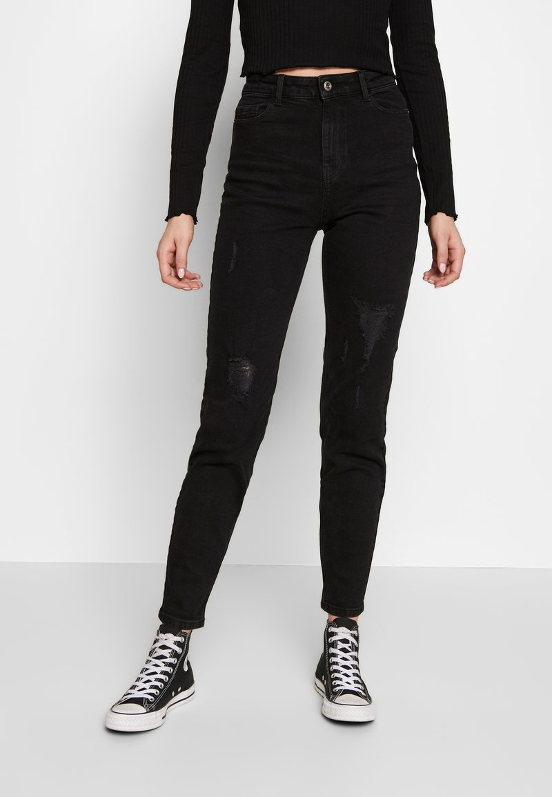 Jeans negros de corte ajustado, de cintura alta y con detalles desgastados en las rodillas. Combinados con zapatillas negras de caña alta y una camiseta negra de canalé.