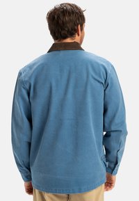 Blue long-sleeve shirt with a brown corduroy collar, featuring buttoned cuffs and a soft fabric texture, viewed from the back.