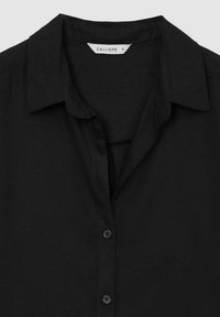 Chemise noire à col avec des boutons sur le devant et une étiquette "Calliope" taille petite à l'intérieur du col.