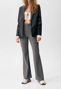 Blazer in pelle nera, top corto color crema, pantaloni grigi svasati e sneakers beige. Le texture combinano elementi lisci, morbidi e su misura.