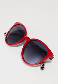 ΚόκκιναOversized γυαλιά ηλίου με gradient σκούρους φακούς, λείο πλαστικό σκελετό και μοτίβο μαύρων και λευκών ακροβραχίων.