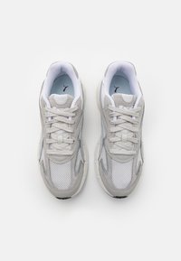 Sneaker grigie e bianche in materiale mesh e suede, con forma arrotondata, lacci e un logo sottile sulla linguetta.