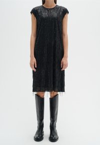 Černé šaty s vertikálními korálky, rovného střihu a s třásněmi na spodním lemu. Nosené s černými kozačkami nad kolena.