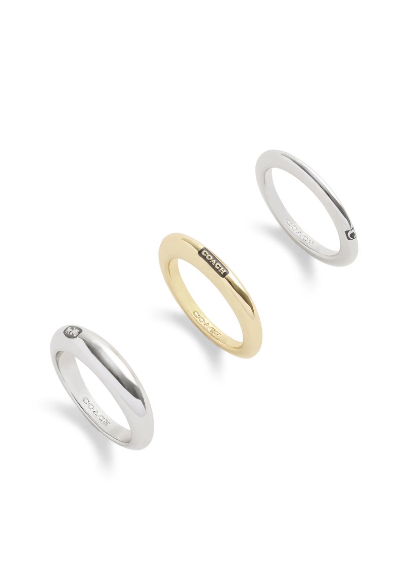 Tres anillos: un anillo de plata pulida a la izquierda, un anillo de oro en el centro con un logotipo negro, y un anillo de plata brillante a la derecha.