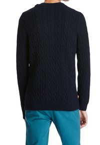 Pull en maille torsadée bleu marine avec un motif texturé, des poignets et un ourlet côtelés. Vue de dos montrant une coupe ajustée et une étiquette orange sur le côté.