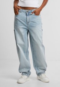 Light blue, loose-fitting denim pants with a high waist, front pockets, and a wide leg design. Worn with white sneakers.