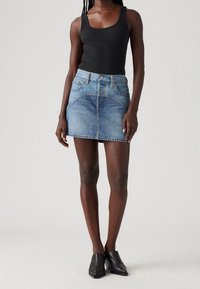 Džínová mini sukně v světle modré barvě se zvýšeným pasem, předními kapsami a jemnými švy. V kombinaci s přiléhavým černým tílkem a černými muly.