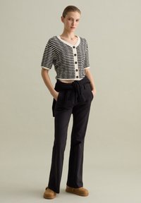 Cardigan corto a righe bianche e nere con maniche corte, dotato di bottoni neri. Abbinato a pantaloni scuri e scarpe slip-on marroni.