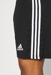 Shorts de sport noirs avec trois bandes blanches sur les côtés. Comprend le logo Adidas en blanc sur le bas de l'ourlet. Tissu léger et texture lisse.