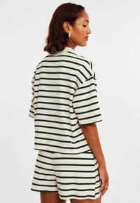 Kortärmad randig topp och shorts-set i krämfärgad och svart ribbad tyg. Har en avslappnad passform, med slitsar på sidorna av toppen och shortsen.