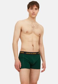 Grüne Baumwoll-Boxershorts mit einem schwarzen Bund, der gelben Logo-Schriftzug zeigt, enganliegendes Design und glatte Textur.