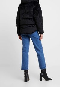 Czarna pikowana kurtka o gładkiej fakturze, zestawiona z niebieskimi prostymi spodniami jeansowymi oraz czarnymi botkami na słupku.