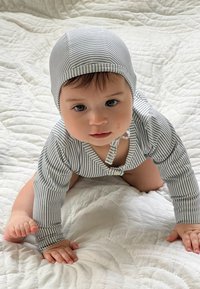 Gestreifter Baby-Body mit passendem Hut, ausgestattet mit einem Druckverschluss und langen Ärmeln, aus weichem Stoff, auf einem gesteppten weißen Hintergrund.