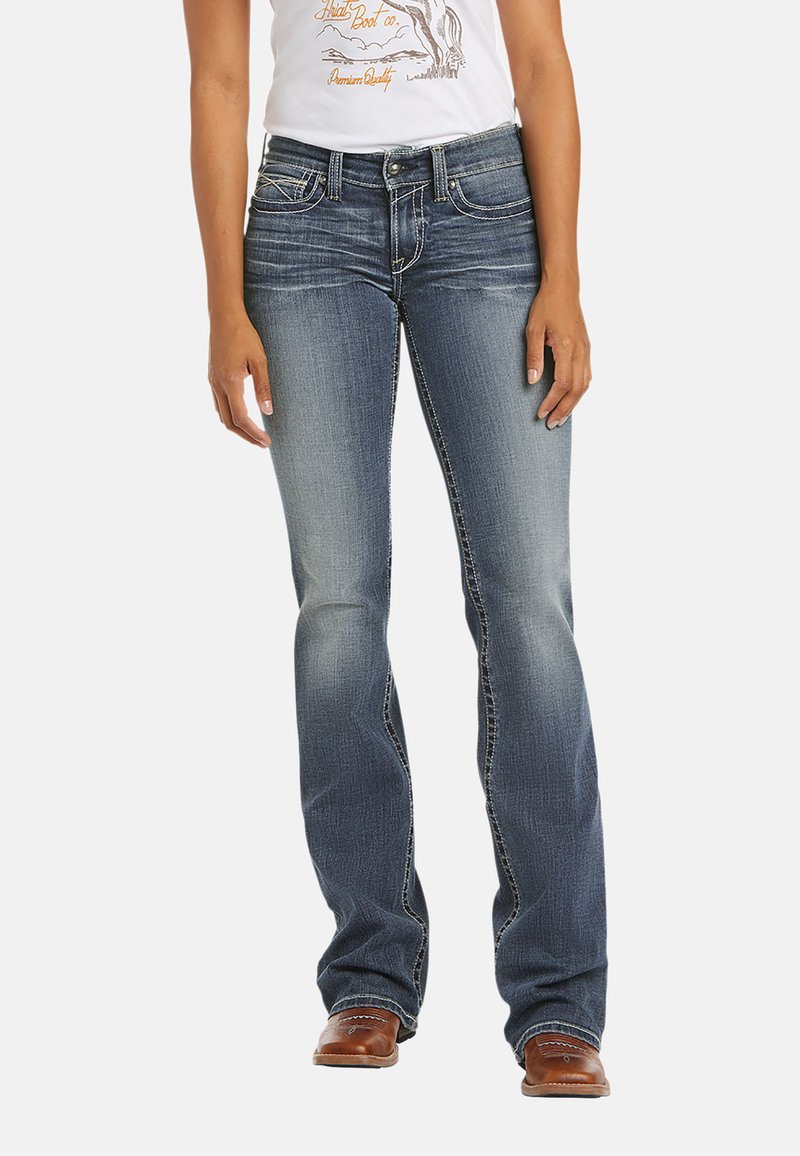 Jeans de mezclilla azul con diseño de pierna acampanada, con costuras en contraste y estilo de cinco bolsillos. Llevados con una camiseta gráfica blanca y botas marrones.