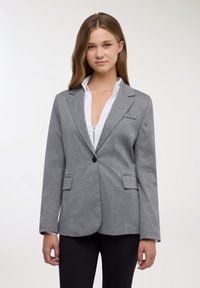 Blazer grigio con texture liscia, chiusura con un solo bottone, rever a incavo e due tasche frontali abbinato a una camicia bianca con colletto.