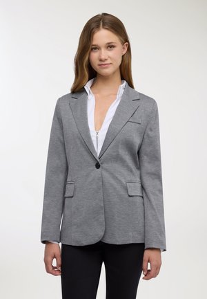 Blazer grigio con texture liscia, chiusura con un solo bottone, rever a incavo e due tasche frontali abbinato a una camicia bianca con colletto.