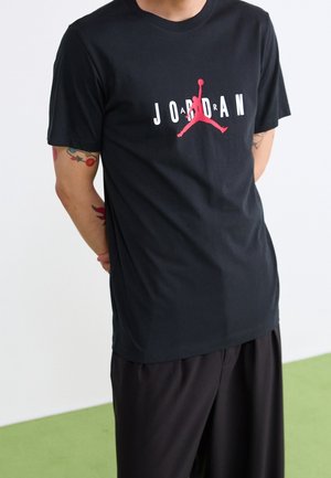 Black cotton t-shirt featuring a large white and red "JORDAN" logo with a silhouette. Short sleeves and a crew neckline. Smooth texture.