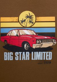Sarkans vintage automašīnas grafiks uz brūna krekla, ar saulrieta fonu, kurā ir dzelteni, zili un melni svītri, blakus palmu kokiem un tekstu.