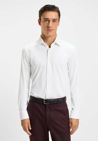 Witte longsleeve blouse met een klassieke kraag en knoopsluiting, gecombineerd met donkerrood marmeren broeken en een zwarte riem. Glad materiaal, strakke pasvorm.