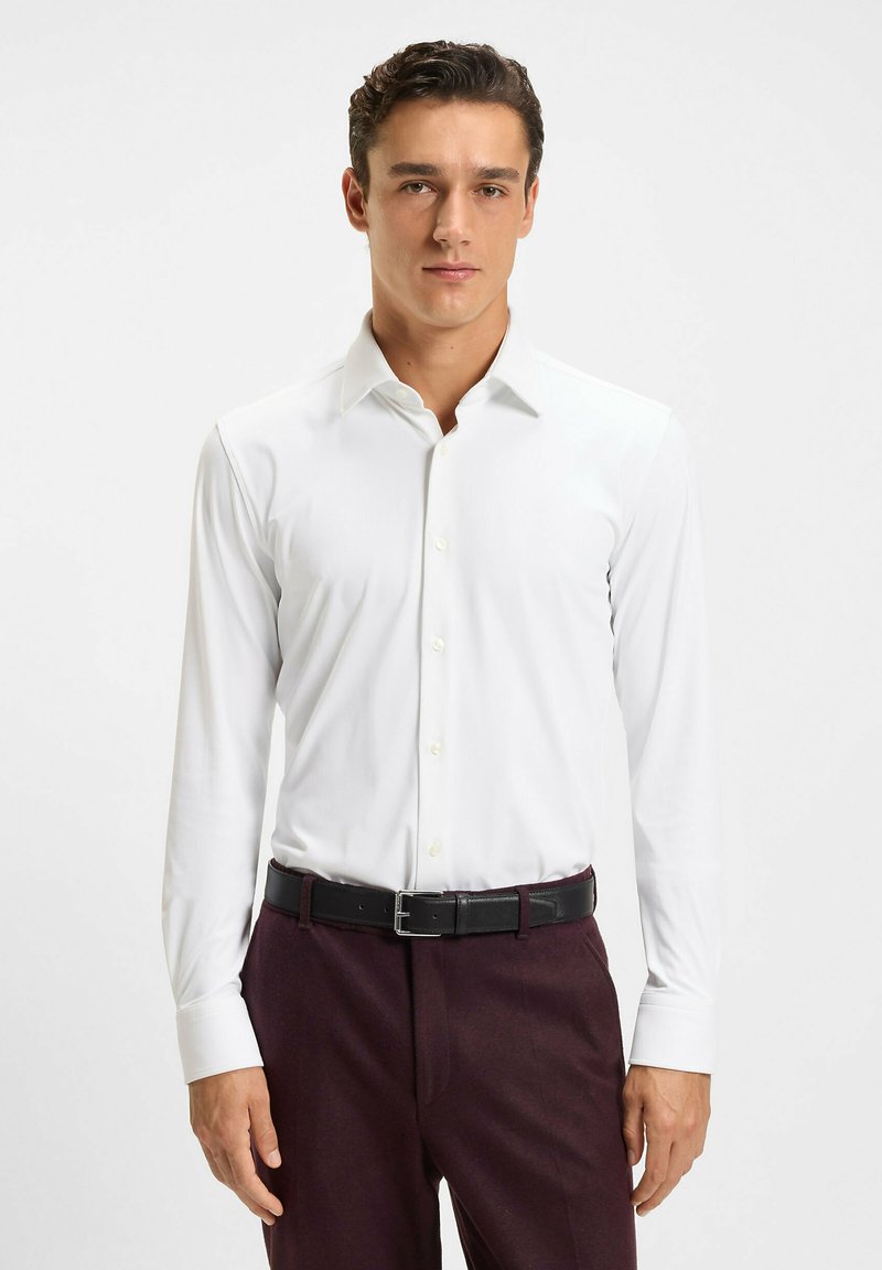 Witte longsleeve blouse met een klassieke kraag en knoopsluiting, gecombineerd met donkerrood marmeren broeken en een zwarte riem. Glad materiaal, strakke pasvorm.