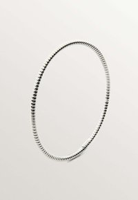Pulsera de bangle en tono plateado con una forma suave y redondeada, textura acanalada y un pequeño logo en un lado.