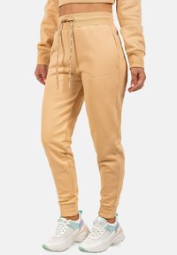 Beige joggingbroek met een trekkoord in de taille, ribgebreide boorden en zijzakken. Kenmerkt zich door een geborduurd logo in een bijpassende kleur.