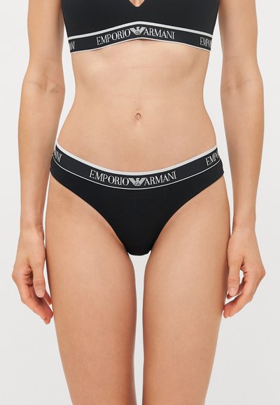 Black Emporio Armani bralette and thong set with elastic band featuring logo in white. Smooth texture and minimalist design without patterns.