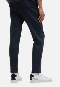 Navy blue sweatpants with a slim fit, made from soft fabric. Paired with white sneakers featuring a black heel and logo detail.