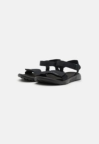 Black sandals with adjustable straps, featuring a textured footbed and a rugged sole for grip, designed for outdoor use.