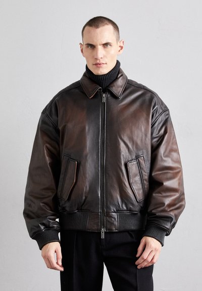 Chaqueta bomber de cuero marrón con cremallera frontal, puños acanalados, dos bolsillos delanteros y un acabado ligeramente texturizado.