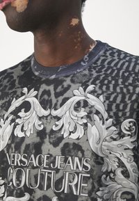 Grafisk t-shirt i grått och svart med ett djurmönster, blommiga detaljer och en ribbad krage med texten "Versace Jeans Couture".