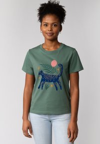 T-shirt en coton vert avec un design de chat marine entouré de spirales, d'étoiles et d'un soleil rose. Manches courtes et col rond.
