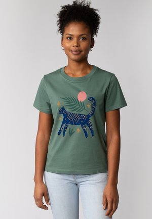 Groene katoenen t-shirt met een ontwerp van een marineblauwe kat met spiralen, sterren en een roze zon. Korte mouwen en een ronde halslijn.