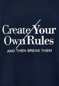 T-shirt in cotone blu navy con testo bianco in grassetto: "Crea le Tue Regole" barrato, seguito da "E POI INFRANGILE."