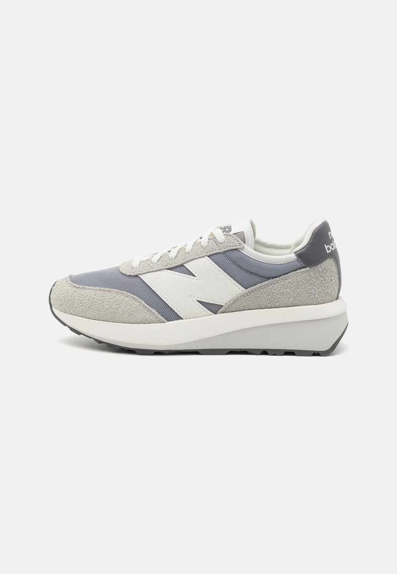 Sapatilhas cinzas e azuis com materiais em camurça e malha, logotipo branco proeminente na lateral, detalhes texturizados e uma entressola branca espessa.