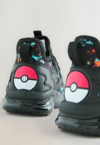 Sorte sneakers med en struktureret overflade, der har et farverigt sprøjmønster og et tydeligt Poké Ball-design på hælen.