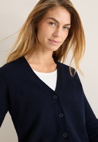 Marinblå cardigan i mjukt tyg, med V-ringning, långa ärmar och fem mörka knappar fram.